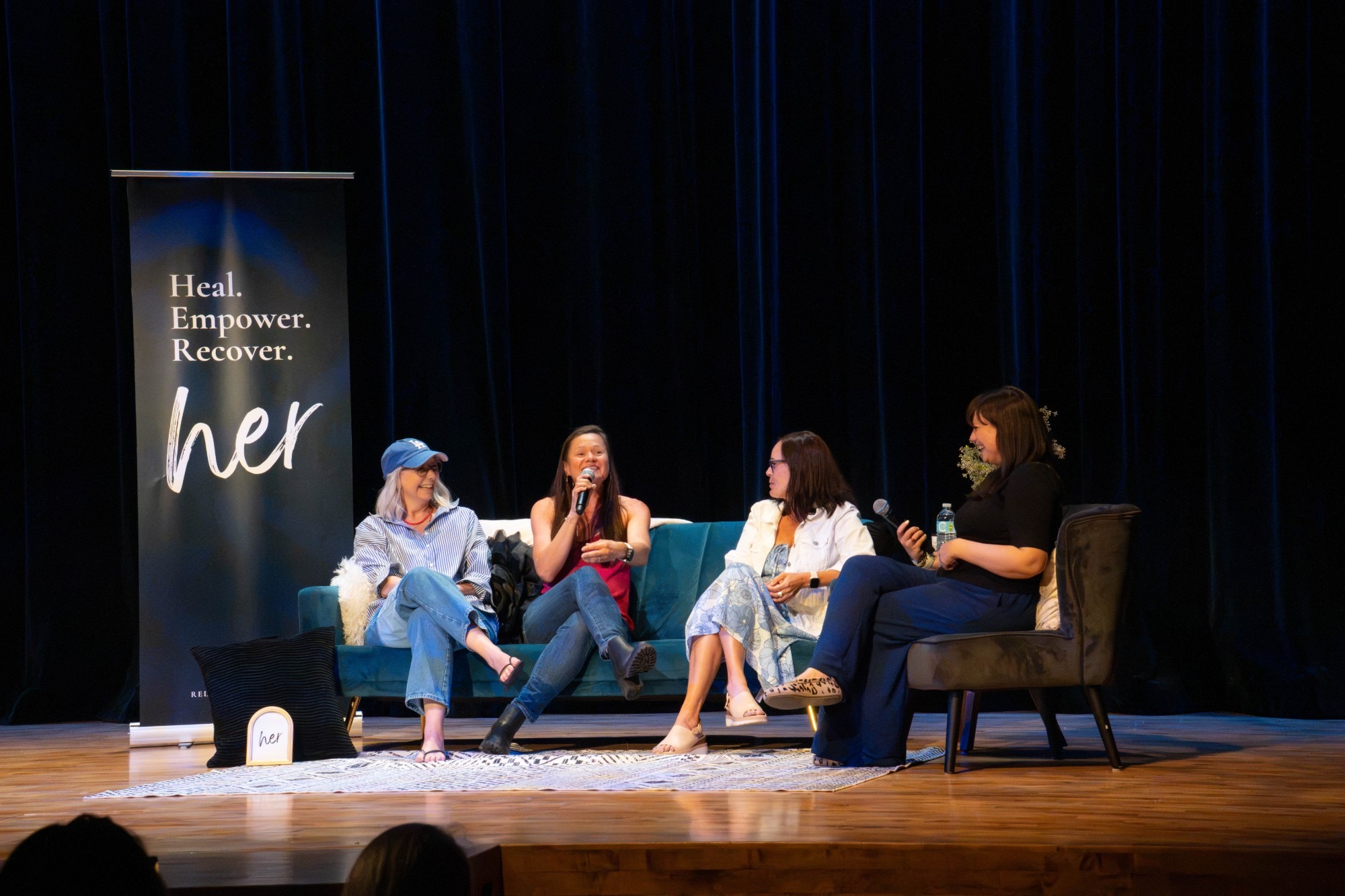 Brooke hosting a live conversation on stage beside the Heal, Empower, Recover banner