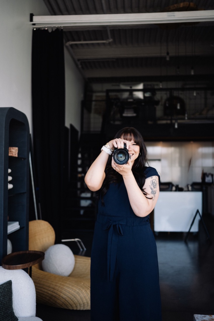 Brooke standing, raising her camera and smiling