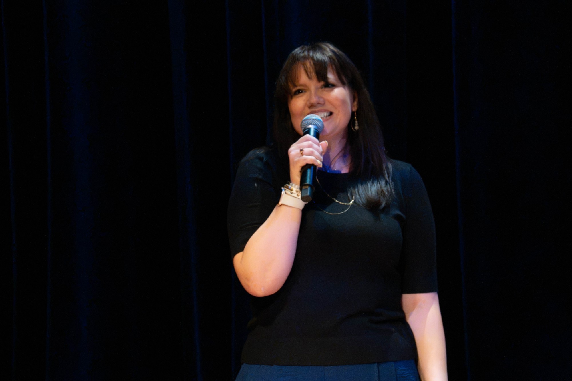 Brooke Redelle smiling as she speaks into a microphone on stage